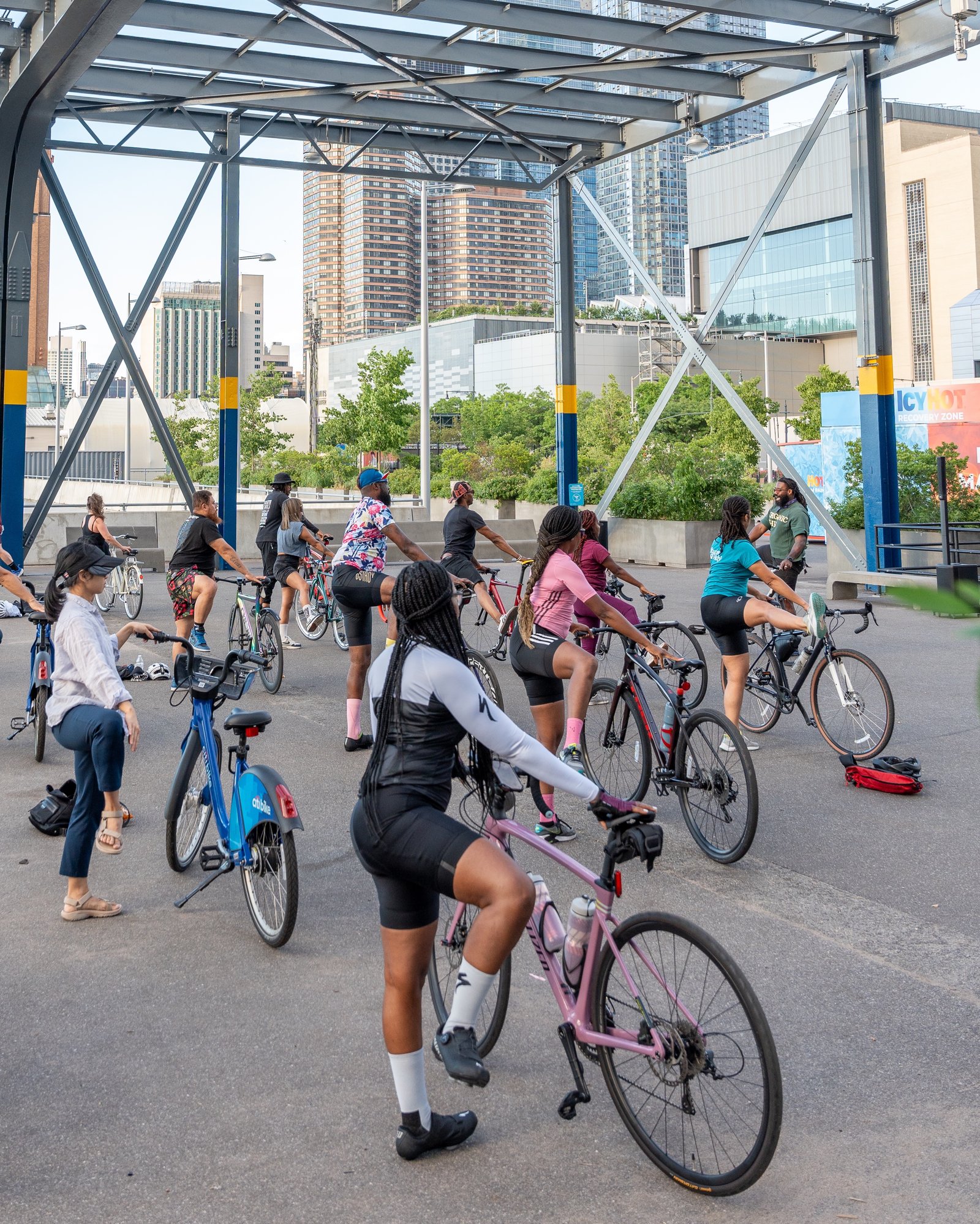 Group bike yoga session with cyclists stretching using their bikes at Pier 76, NYC skyline in background