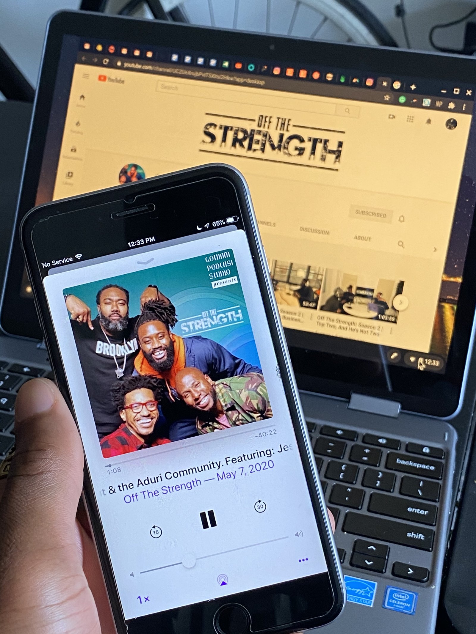 Phone playing an Off The Strength episode with the YouTube channel open on a laptop behind it