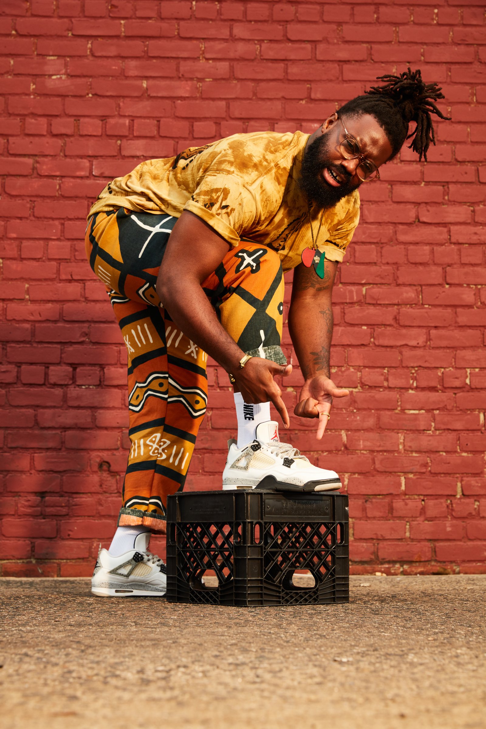 Posing with a foot on a milk crate against a red brick wall