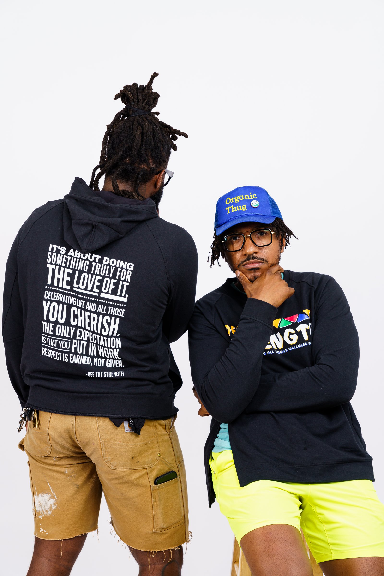 Two people showing off Off The Strength branded hoodie and cap merchandise