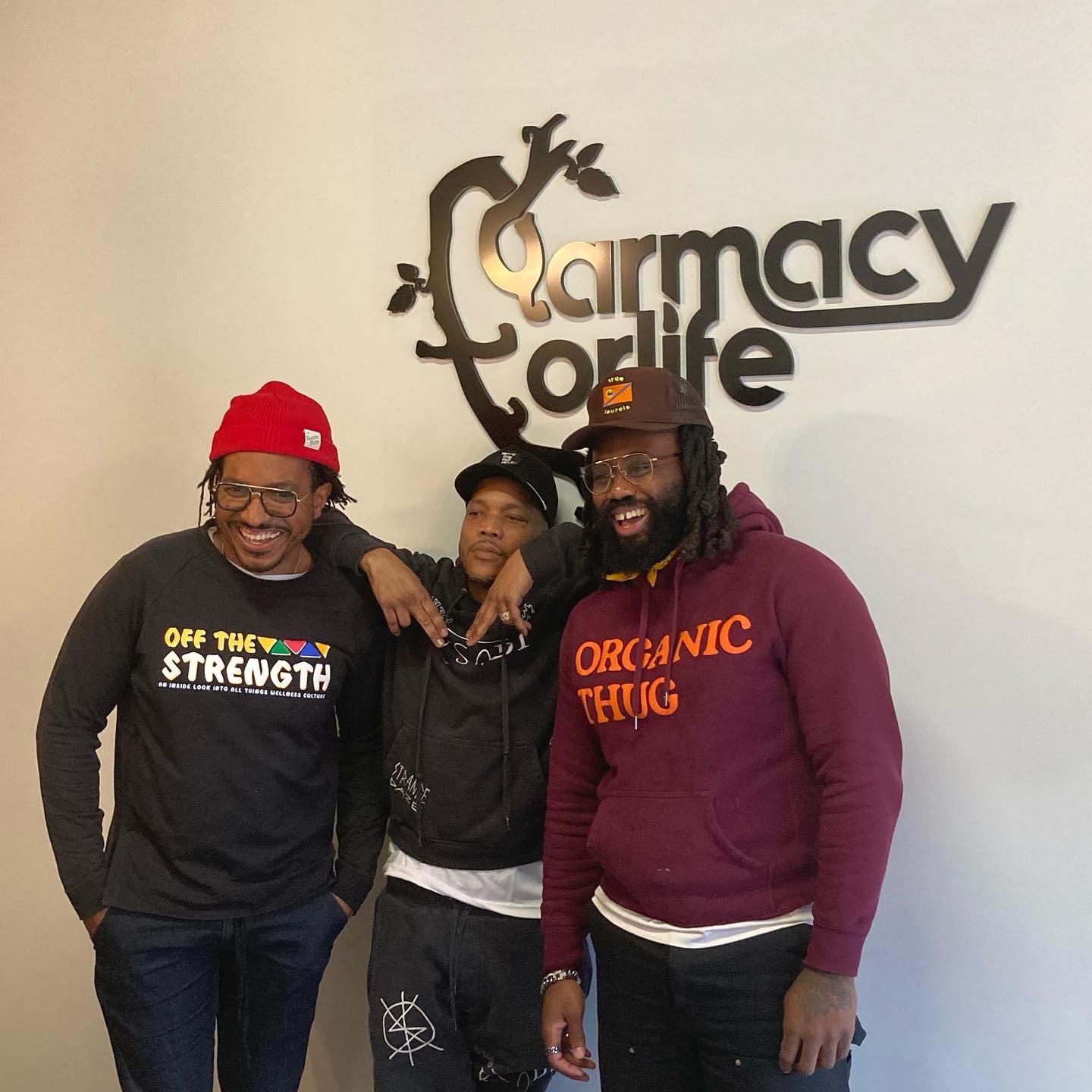 Group photo wearing Off The Strength and Organic Thug branded apparel in front of a Pharmacy for Life sign
