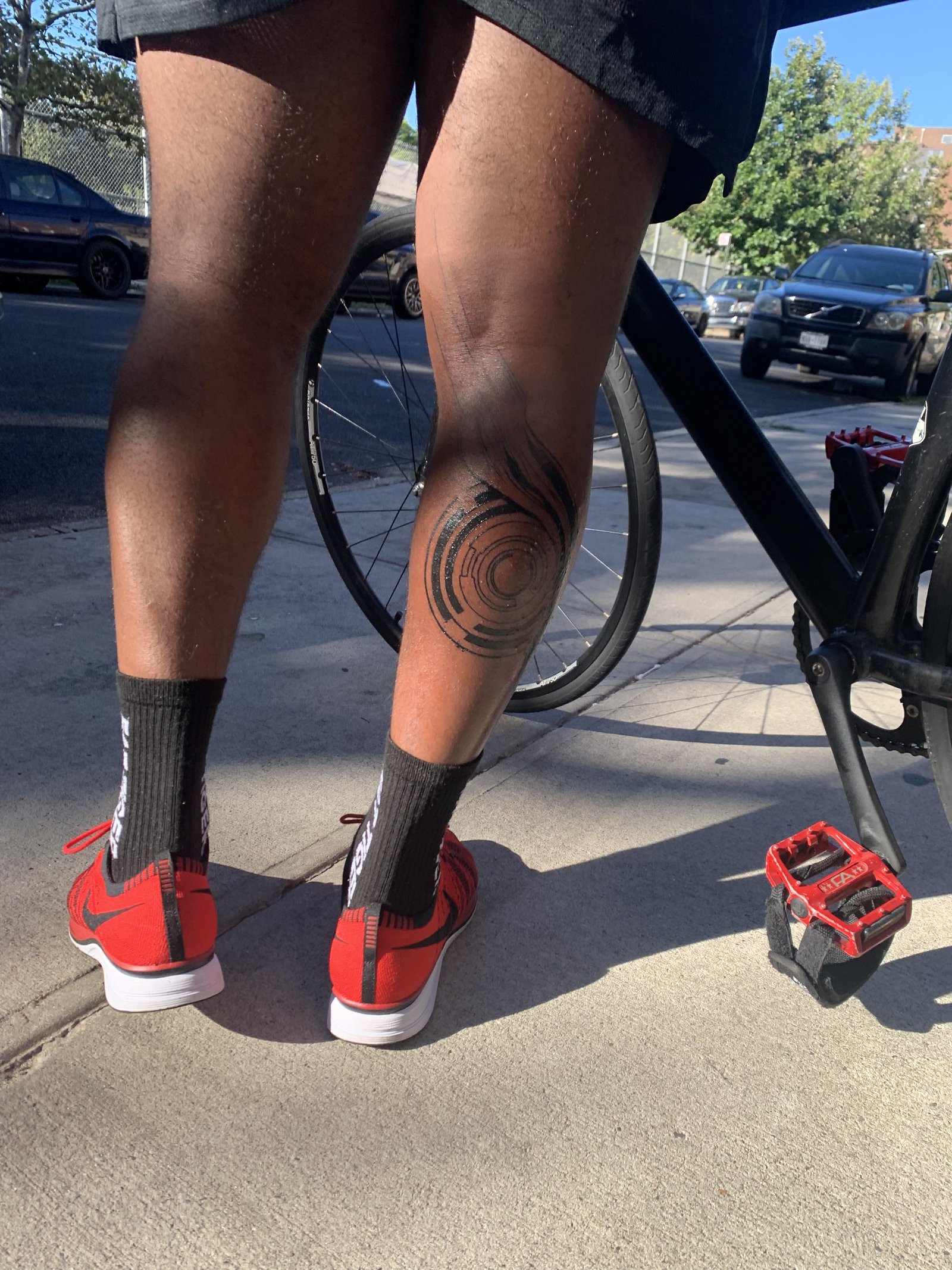 Standing beside a bike outdoors, showing the healed leg tattoo from behind
