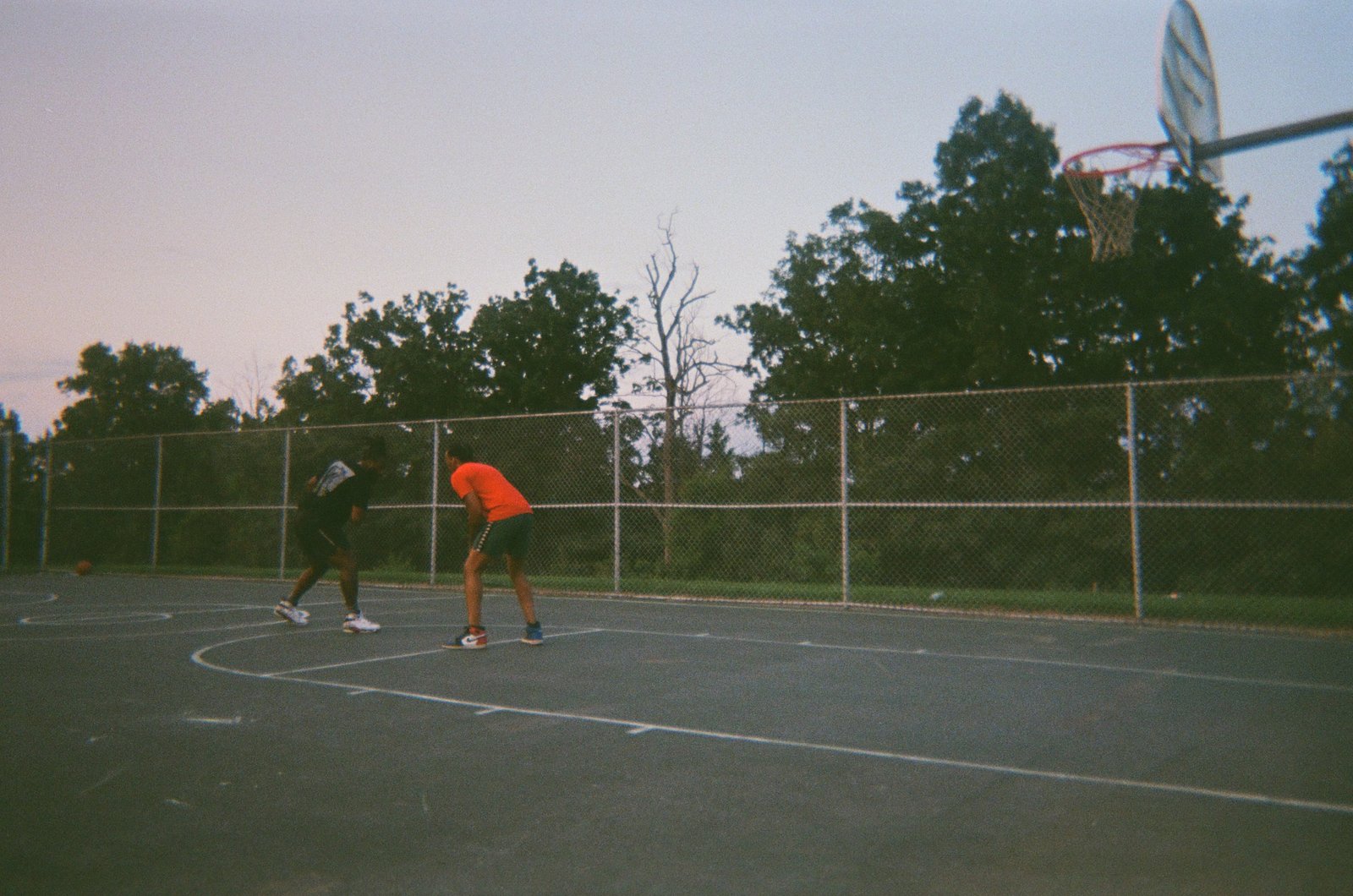 Playing basketball outdoors at dusk with a friend