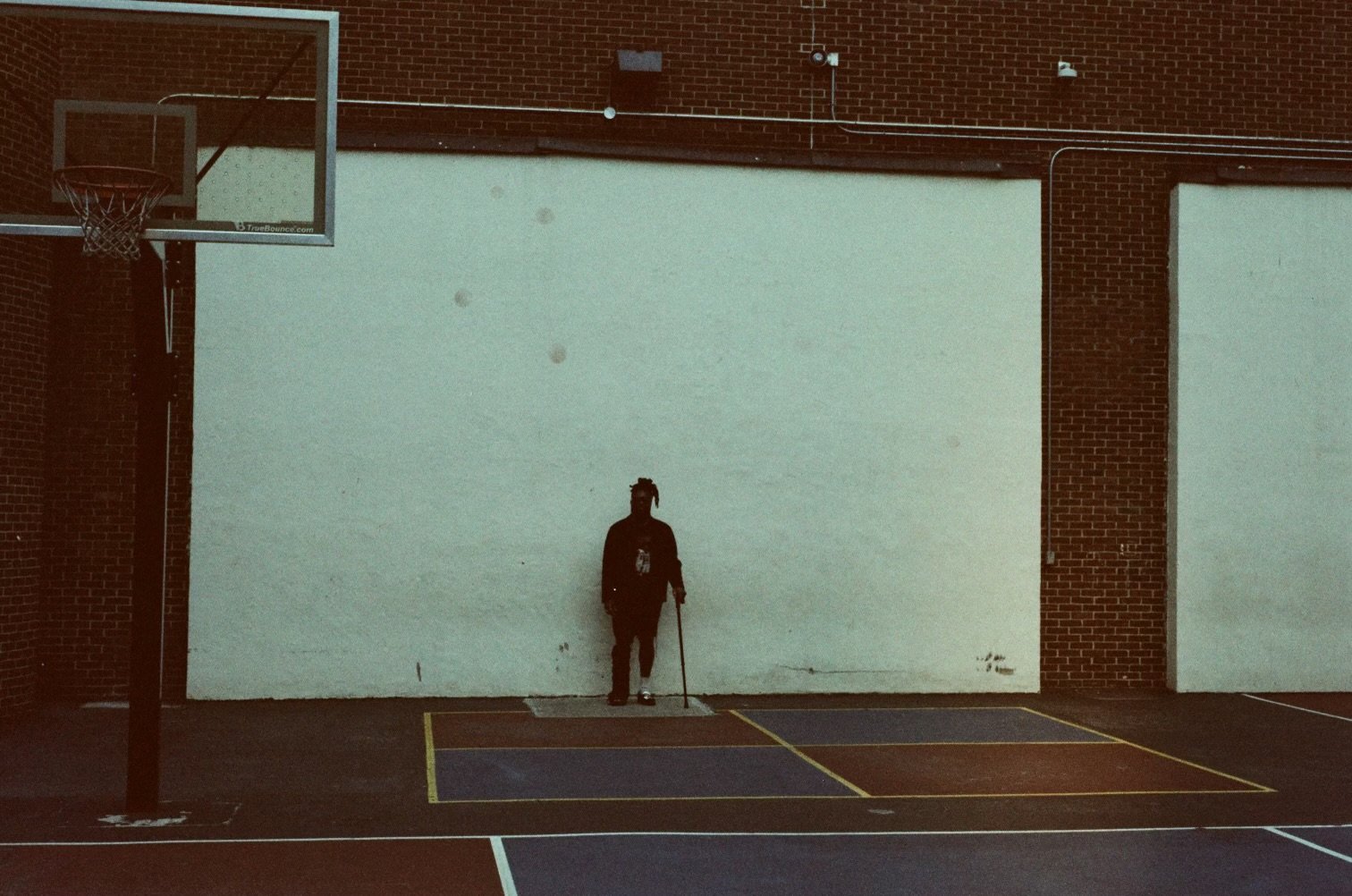 Silhouette standing with a cane in front of a wall on a basketball court