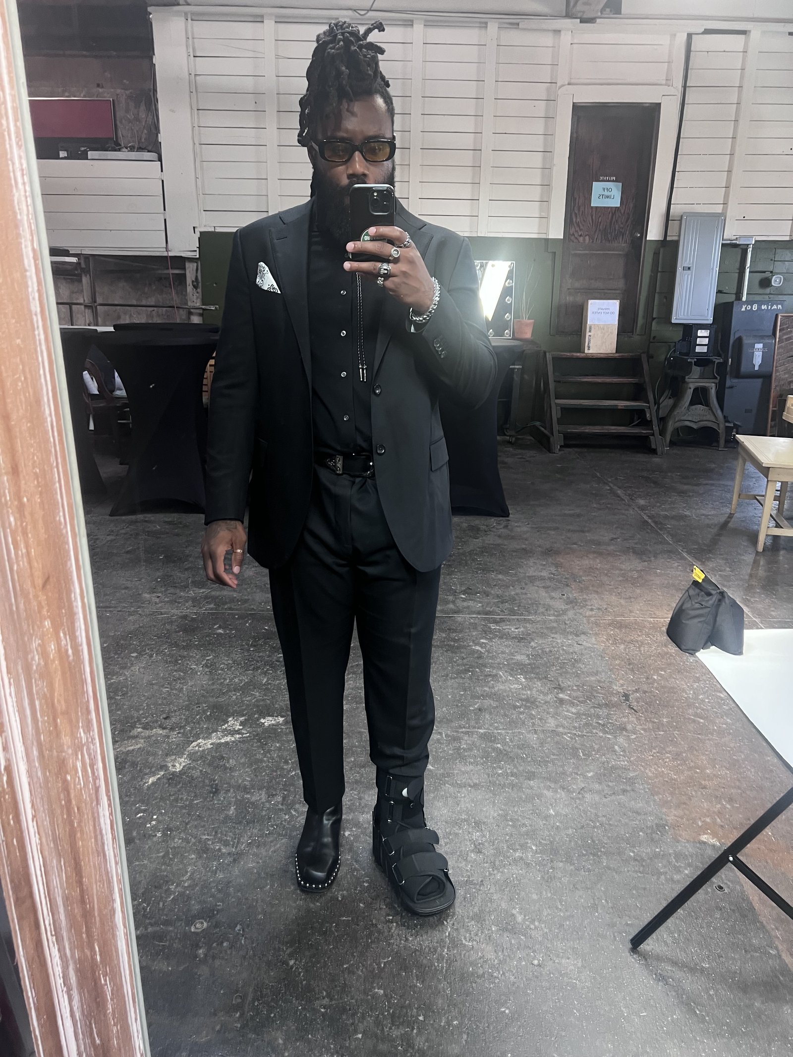 Mirror selfie in a black suit, wearing a walking boot