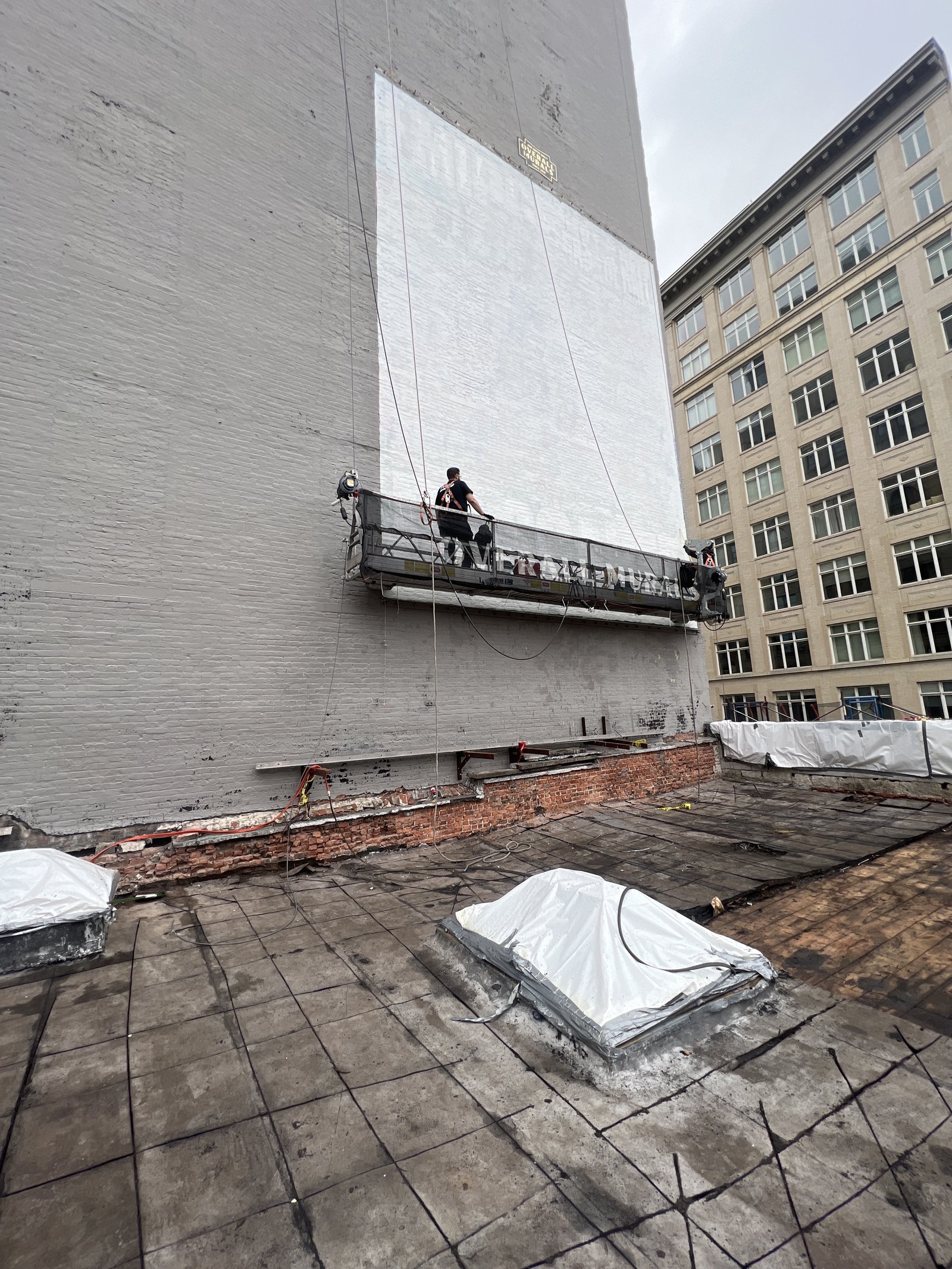 Painter suspended on a rig, hand-painting a large building mural